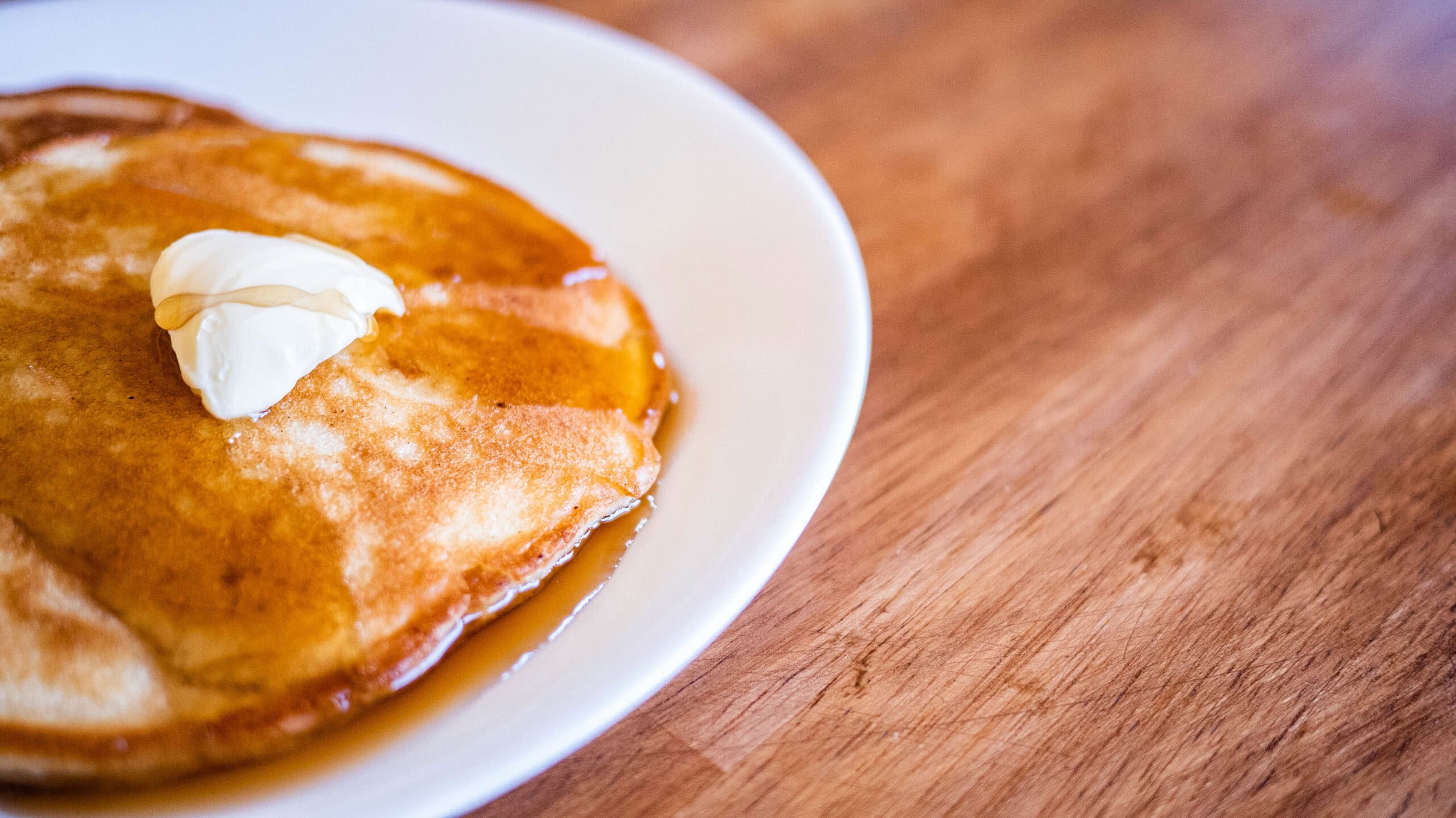 A white plate with a pancake that has a dollop of butter and syrup.